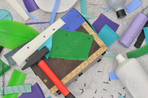 Reusing multicolored plastic bottles and using them as a colorful mosaic. Top view work table and shallow depth of field. Black and red hammer, nails and a pot cover 
during mosaic covering. Upcycling