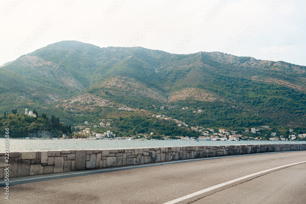 Fototapeta premium Mountain view along a road near water with houses in the distance at sunset