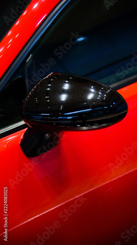 Close-up of a glossy black side mirror on a modern red sports car.