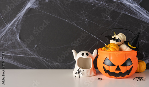 Happy Halloween celebration with pumpkin bucket, ghost decoration, spiders and witch hat on cobweb background on wide banner wall and table background