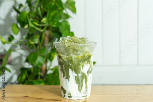 barista prepares a delicious iced Iced matcha green tea with fresh milk or Matcha latte in plastic glass and shop beverage for the menu on table.