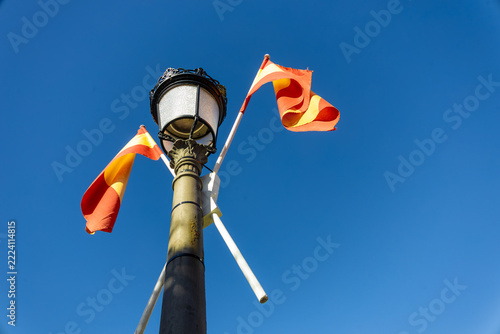 Spanish flags attached to a classic street lamp against a clear blue sky