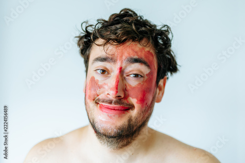 Smiling man with colorful face paint looking at camera. Playful studio portrait and happy humor