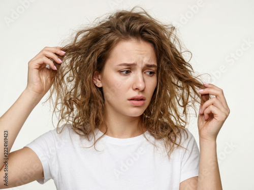 Young woman looking concerned at her dry frizzy hair isolated on white background