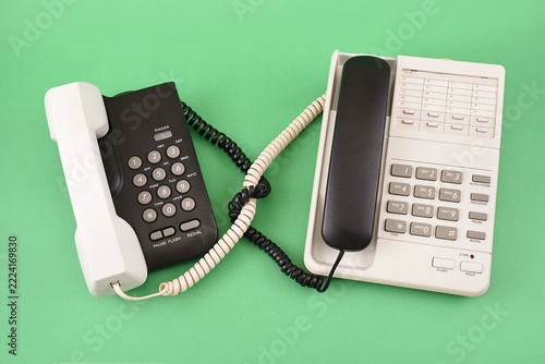 Retro black and white telephones with entangled cords and swapped handsets on a green background. Top view. Concept of communication, mixed signals and relationships.