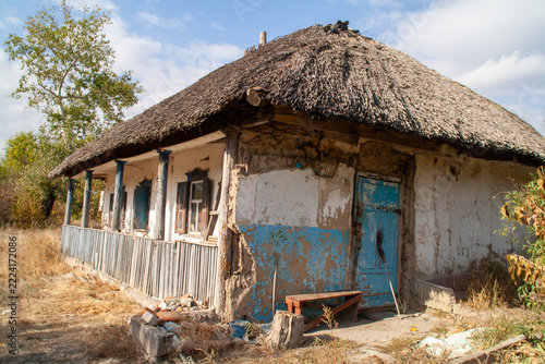 Traditional Ukrainian thatched roof mud hut with weathered blue door and porch in rural setting