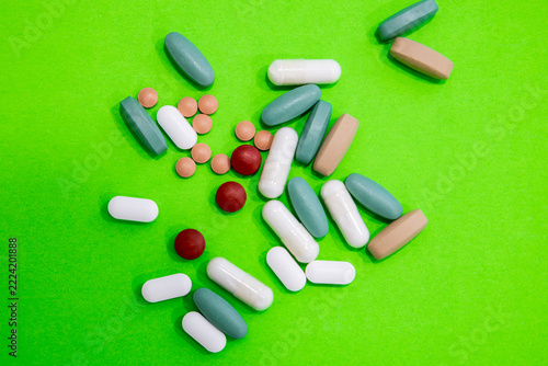 High angle view of scattering of different pills in several sizes, colours and shapes on bright green background