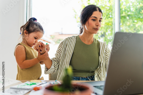 A mother works on a laptop while her daughter distracts her
