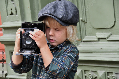 Boy in a flat cap holding an antique camera, vintage photography and historical style