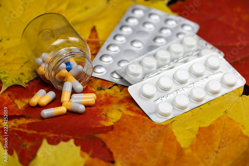 Pills on yellow and red maple leaves, bottle of capsules and tablets in blister packs. Concept of nutrition supplements, antidepressants, vitamins for immunity in autumn flu season