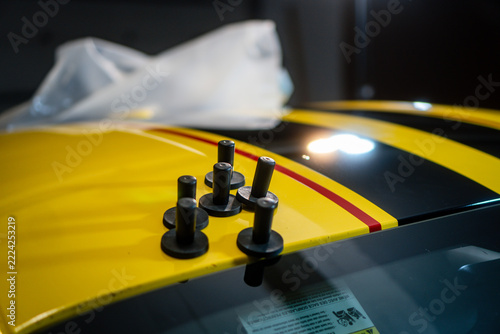 Close-up of magnets used during car wrapping on a yellow sports car, captured while installing black racing stripes with red pinstriping