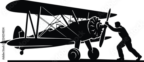 Silhouette of a mechanic starting a vintage biplane propeller airplane