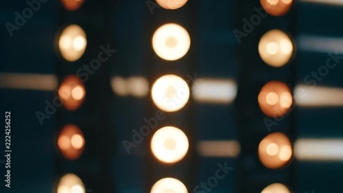 Vertical rows of glowing vintage studio spotlights illuminating dark background during theatrical event