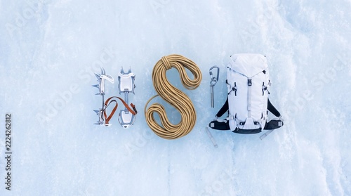 Top down overhead view of professional mountaineering and ice climbing equipment including technical rope, crampons, ice screw, and backpack neatly organized on a frozen ice surface background.