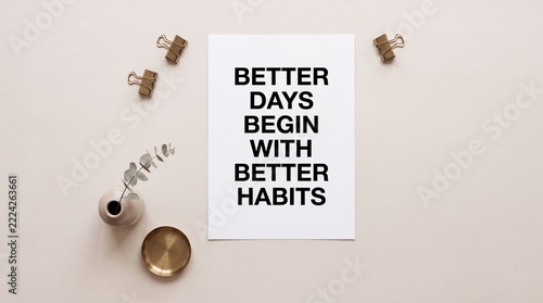 Top down view of a motivational quote Better Days Begin With Better Habits printed on white paper surrounded by minimalist stationery, gold bowl, and plant on beige background for productivity.