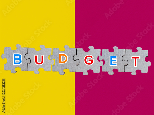 Budget Word Spelled on Jigsaw Puzzle Pieces over Yellow and Magenta Split Background for Financial Planning Concept