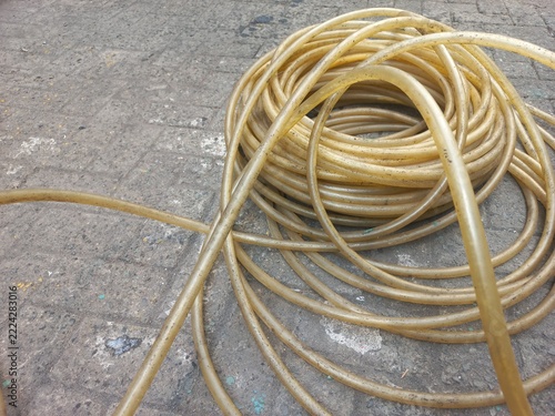 Coiled transparent yellow plastic water hose on a paved courtyard floor.