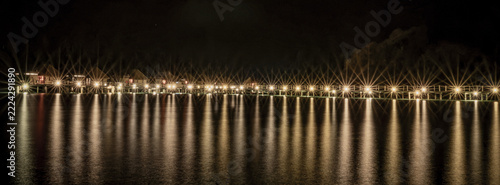 Fotografie View of the illuminated overwater bungalows at Likuliku Lagoon Resort with bright lights reflecting on the calm ocean water at night in Yaro, Nadroga-Navosa, Fiji