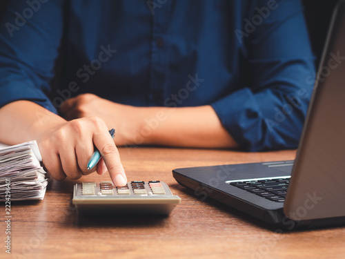 Person pressing calculator beside laptop and documents