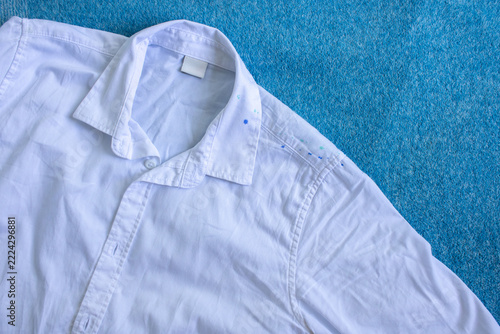 A white shirt with blue paint stains lying on a blue throw blanket. Concept of garment care and accidental ink staining.