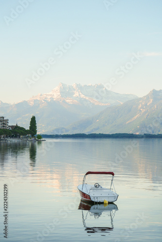 Small moored boat beside buoy on still lake with snowy mountain reflections