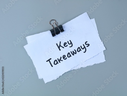 White paper note with the handwritten text Key takeaways attached by a black clip on a gray background, perfect for business concepts, meetings, education, presentations, and corporate summaries