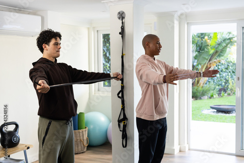 African American men in hoodies and sweats using resistance band near suspension straps in home gym