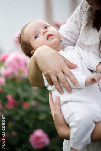 Cute newborn baby in mother hands close up among flowers in the garden. Love, care and family in countryside concept. Happy Mothers day! Adoption and maternity
