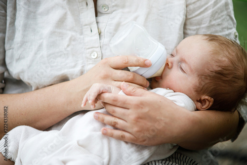 Mother feeding cute newborn baby with bottle close up in the garden. Love, care and family in countryside concept. Happy Mothers day! Adoption and maternity