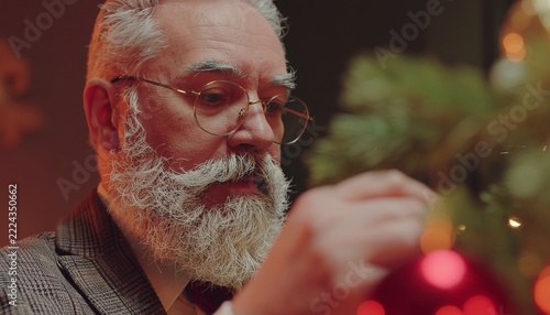 Senior man with white beard and classes decorating a Christmas tree 