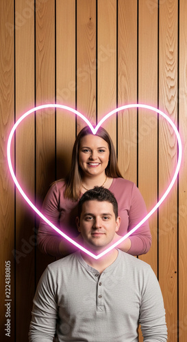 Couple framed by a neon heart against a wood paneled background, symbolizing love and Valentine's Day
