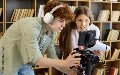 Students filmmakers teamwork in library video production. Young crew sets camera rig, tests audio and reviews script pages for education learning project. Focused concept of education teamwork