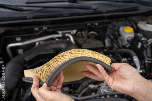 Hands hold dirty air filter above engine bay