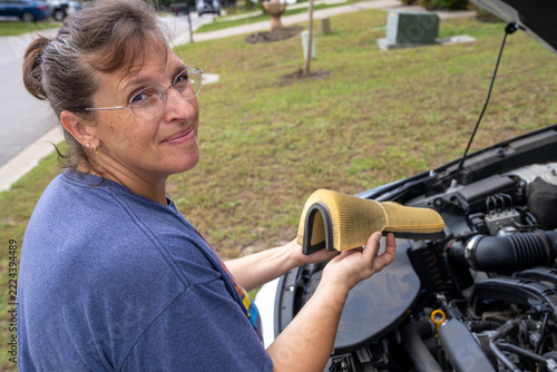 Woman holds car air filter near open engine bay