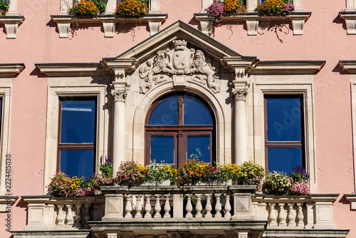 Historic town hall facade in Kaufbeuren, Bavaria, Germany with ornate balcony, stone lion coat of arms and colorful summer flower boxes on pink wall