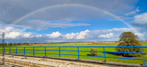 Rainbow over rural countryside near River Waal in The Netherlands, known as floodplain, seen from blue railed bridge.