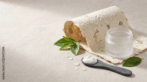 Natural skincare cream jar with green leaves on beige background