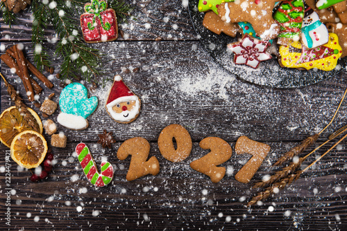 Top view holiday baking concept. Colorful iced biscuits like santa and candy canes with cinnamon and fir on a rustic table dusted with powdered sugar snow. Cozy and festive winter celebration