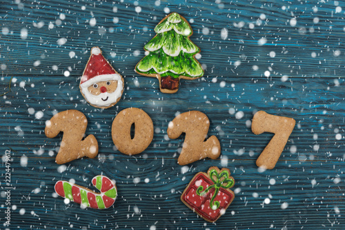 Top view holiday baking concept. Colorful iced biscuits like santa and candy canes with cinnamon and fir on a rustic table dusted with powdered sugar snow. Cozy and festive winter celebration