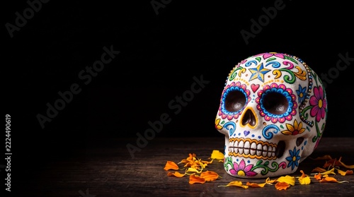 Día de Muertos celebration background featuring a traditional decorated sugar skull and marigold flower petals on a dark wooden table with copy space