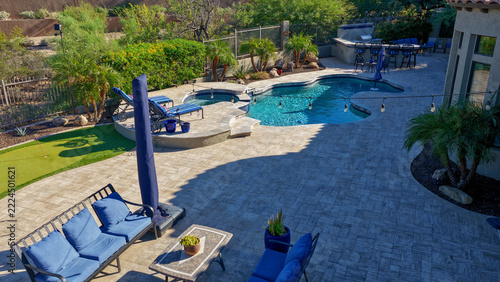 4K aerial view of a luxury Arizona desert landscaped backyard featuring a saltwater swimming pool, spa, outdoor BBQ kitchen, fireplace, putting green and low-maintenance landscaping.