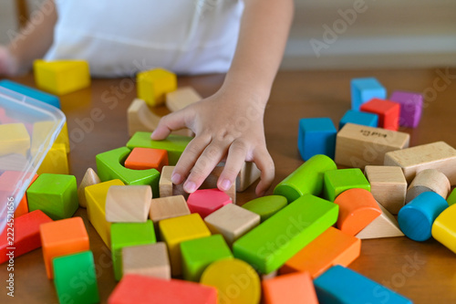Colorful Children’s Building Blocks on Table with Small Hand Reaching for Shapes to Encourage Creativity and Motor Skills in Early Development Stages