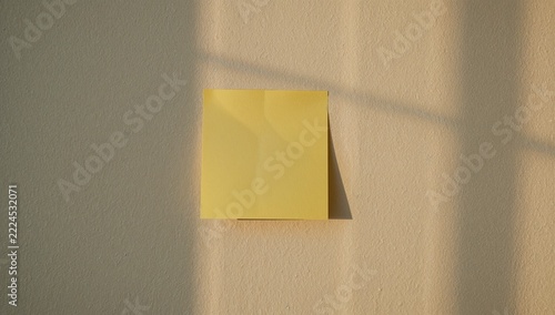 A yellow post-it note stuck on a wall next to a window, simple and clear
