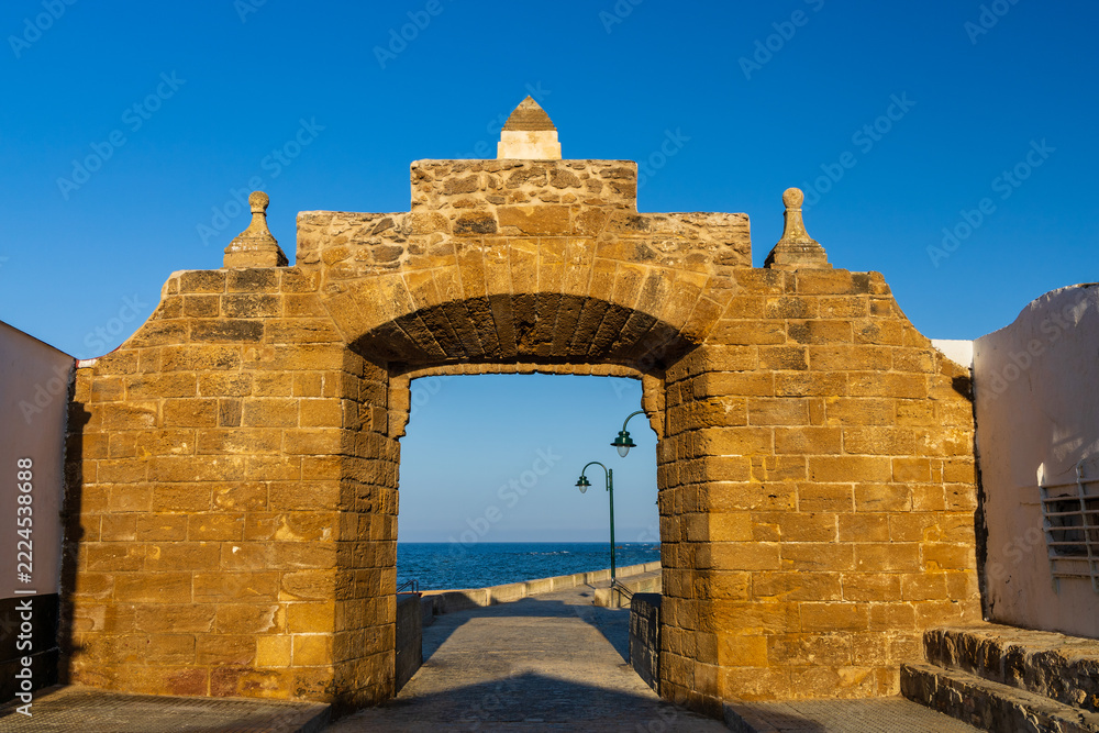 Naklejka premium Historic stone wall of Puerta de la Caleta with an archway leading to the causeway toward San Sebastian Castle in Cadiz, Andalusia, Spain.