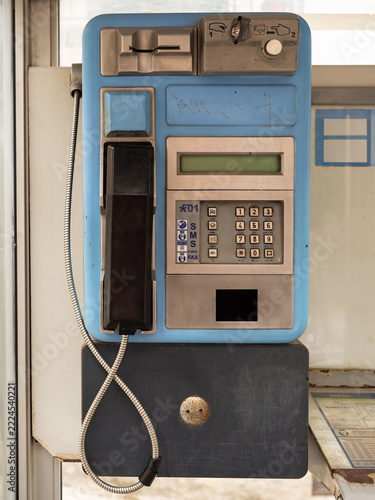 A vintage blue public payphone mounted on a wall with a black handset and an analog keypad