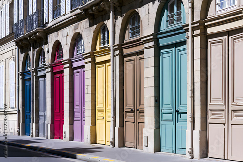 Vibrant colorful doors and classic windows on a historic European building facade, showcasing ornate architectural details and varying shutter styles.