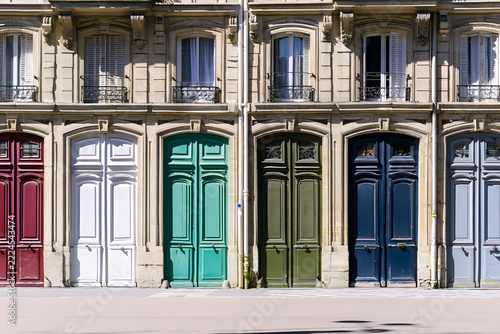 Vibrant colorful doors and classic windows on a historic European building facade, showcasing ornate architectural details and varying shutter styles.