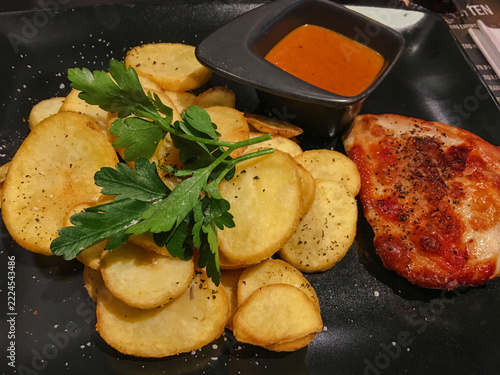 Fried potato slices with parsley, grilled meat and sauce on plate