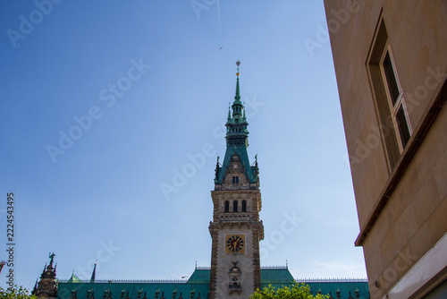 Town hall spire and clock beside a stone building, Hamburg, Germany