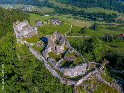 Aerial view of the historic Ruine Alt Bechburg castle ruins, featuring stone walls and crumbling towers surrounded by lush green forests and rolling hills in Holderbank, Solothurn, Switzerland.